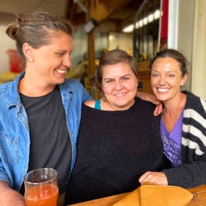 Three women smiling at camera with beer